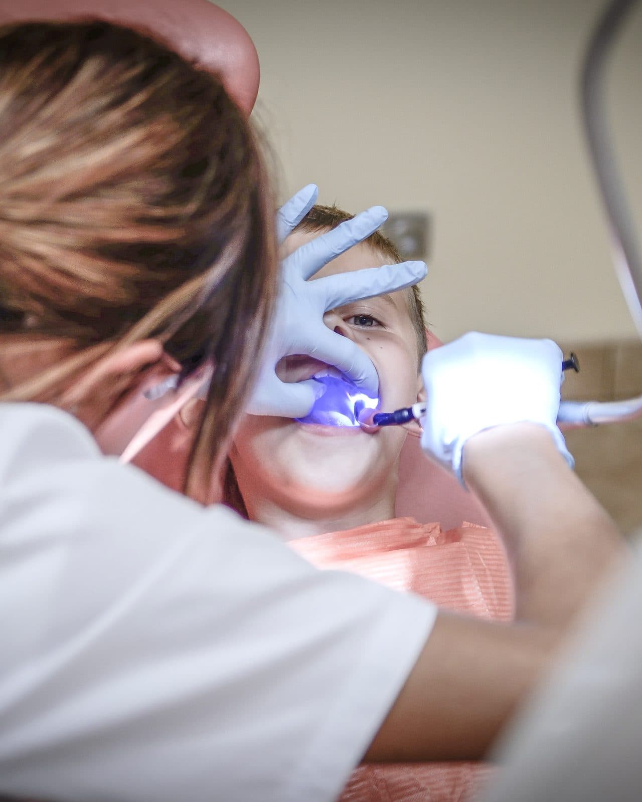 A dental assistant using a blue curing light on a young patient